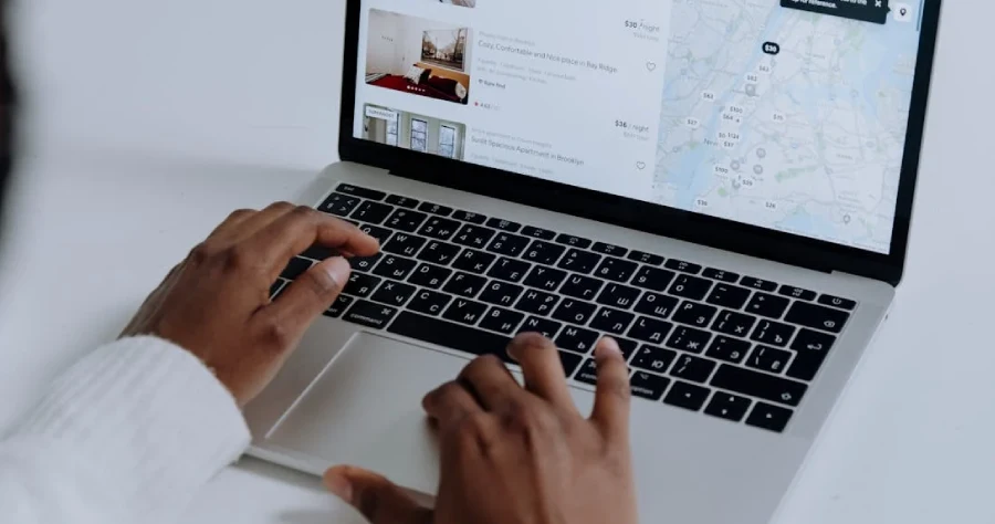 a photo showing a hand of a person listing his house online, facing a laptop