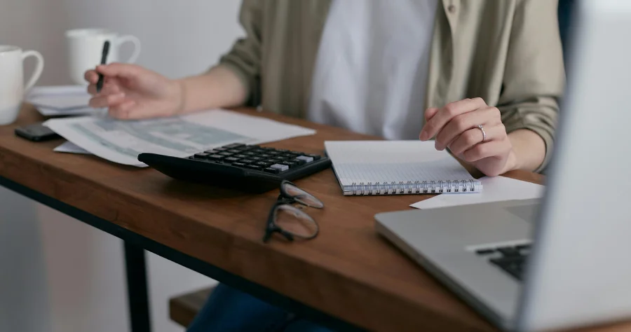 hand of a woman writing in a desk with papers and a laptop